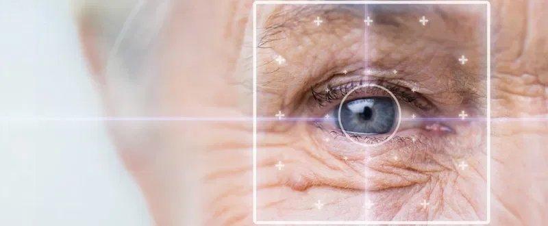 Close-up of an older person's eye with visible wrinkles, surrounded by a digital interface overlay, including crosshairs and lines, suggesting a ray-tracing LASIK scan or topography-guided laser correction for precise vision testing.