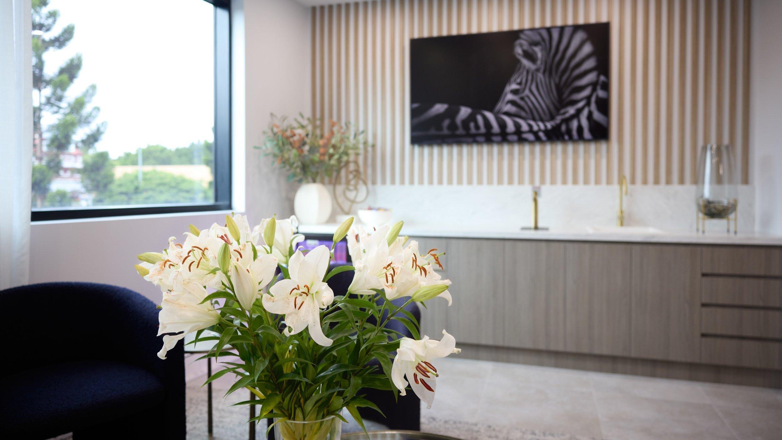 A modern, bright room with a bouquet of white lilies on a table, a black armchair, and zebra artwork on a striped accent wall—this stylish space is proof that laser eye myths debunked can inspire bold, contemporary interiors.