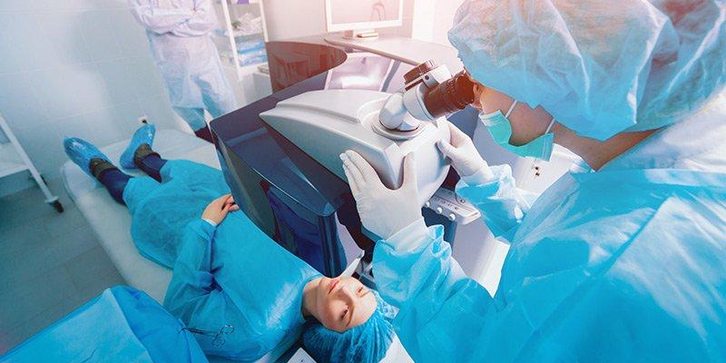 A patient lies on an operating table as a surgeon in blue scrubs and a mask uses advanced technology to perform laser eye surgery, aiming to restore crystal-clear vision in a modern medical clinic.