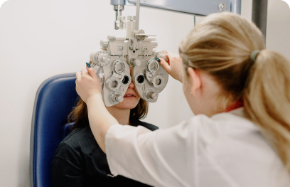 A woman undergoes an eye exam as an optometrist adjusts a phoropter in front of her face to test her vision and discuss potential vision correction options.